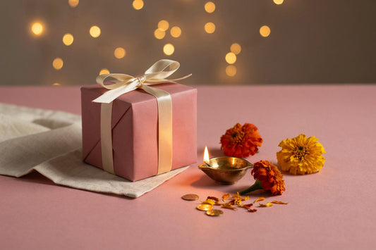 Pink-wrapped gift box with a lit diya and marigold flowers