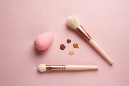 Makeup sponge and brushes with foundation drops on a pink surface