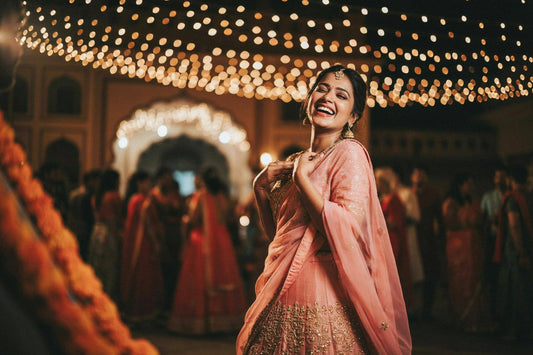 Wedding guest in a pink lehenga laughing under fairy lights